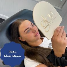 a woman sitting in a chair holding up a mirror with the words real glass mirror on it