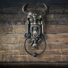 a metal mask mounted to the side of a wooden wall with an iron ring on it