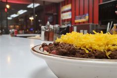 a bowl filled with chili and cheese on top of a table in front of a restaurant