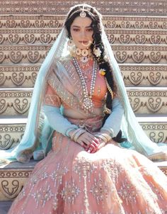 a woman sitting on some steps wearing a pink and blue dress with pearls in her hair