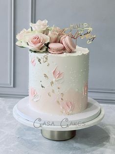 a white cake with pink flowers and macaroons on top