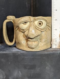 a ceramic mug with a face on it next to a ruler