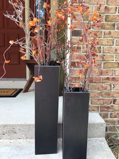 two tall black vases sitting on top of a cement slab next to a door