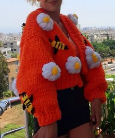 a woman wearing an orange cardigan with bees on the front and flowers on the back