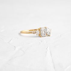 an engagement ring with three stones on it, sitting on top of a white surface