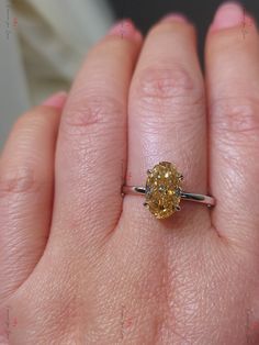 a close up of a person's hand holding a ring with a yellow diamond