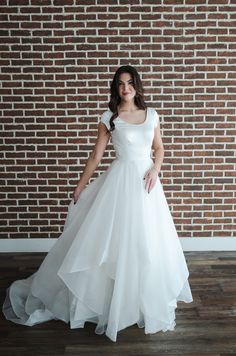 a woman standing in front of a brick wall wearing a white wedding dress with short sleeves