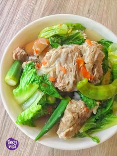 a white bowl filled with meat and vegetables on top of a wooden table next to a fork