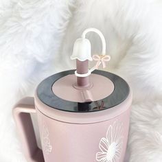 a pink coffee mug with a white flower on the top and a light blue lid