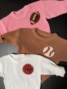 three sweaters with different designs on them sitting on top of a black table next to each other