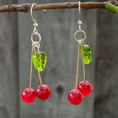 two cherries hanging from a branch with green and red beads on it's hooks