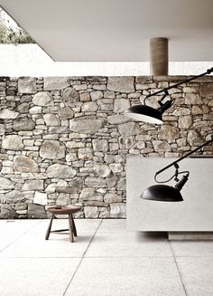 a stone wall with two black lamps on it and a stool in front of it