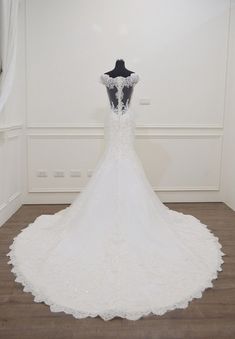 the back of a wedding dress on display in a room with white walls and wood flooring