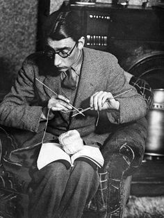 a man sitting in a chair knitting on a pair of yarns with his hands