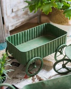 a green wagon sitting on top of a table next to a potted plant and wheelbarrow