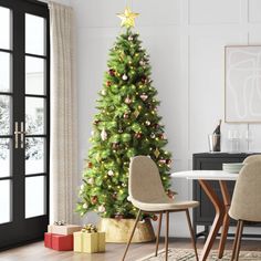 a decorated christmas tree in the corner of a room with two chairs and a table