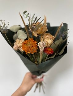 a hand holding a bouquet of flowers on a white background with an orange and yellow flower