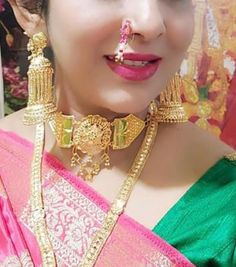 a woman in a green and pink saree with gold jewelry on her face, wearing a nose ring