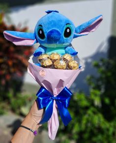 someone holding up a small stuffed animal with chocolates in it's mouth and wrapped in blue ribbon