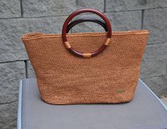 La borsa tote di rafia di viscosa lucida con i manici di legno foderata con il tessuto di cotone. Al interno della borsa ci sono due tasche (una con la cerniera).  Le misure dello sfondo 8,5×26 cm. L'altezza della borsa è 22 cm. I macini sono rotondi del diametro di 14 cm. Brown Top Handle Beach Bag With Bamboo Handle, Natural Straw Bag With Round Handle For Shopping, Summer Straw Bag With Round Handle For Shopping, Beach Straw Bag With Round Handles, Brown Woven Beach Bag With Round Handle, Natural Color Straw Bag With Round Handle For Shopping, Brown Crochet Jute Bag With Top Handle, Daily Use Brown Beach Bag With Round Handle, Vacation Beach Bag With Round Handles