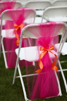 rows of white folding chairs with pink and orange sashes tied to the back of them