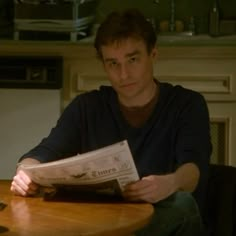 a man sitting at a table with a newspaper in his hand and a cup on the table