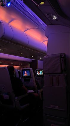 the inside of an airplane with purple lighting and people sitting in seats watching televisions