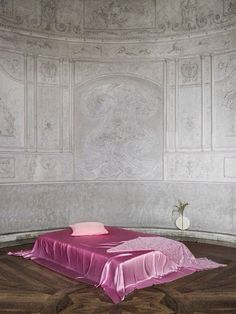 a bed with a pink blanket on top of it in front of a white wall