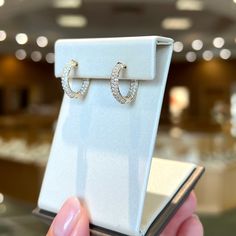 a pair of diamond hoop earrings is being held by a woman's hand in front of a jewelry box