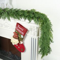 a christmas stocking is hanging on the mantel above a fireplace with greenery