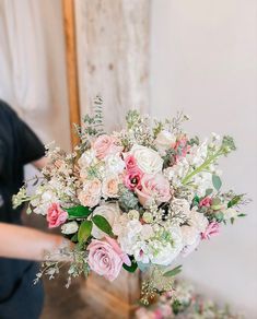 a bouquet of flowers sitting on top of a wooden table next to a person standing in front of a mirror