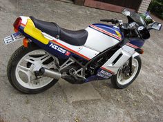 a motorcycle parked on the side of a road next to a garage door and trees