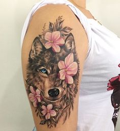 a woman's arm with a wolf and flowers tattoo on her left shoulder, next to a pink flower