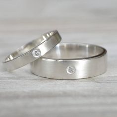 two white gold wedding rings with diamonds on them sitting on top of a wooden table