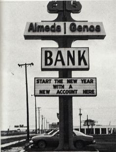 a black and white photo of a bank sign with cars parked in the parking lot