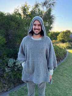 a man standing in the grass wearing a gray sweater