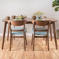 two wooden chairs sitting at a table with plates and cups on it in front of a potted plant