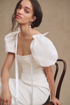 a woman in a white dress sitting on a chair with her head turned to the side