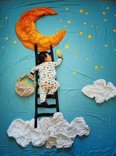 a child laying on top of a ladder next to an orange moon and stars decoration