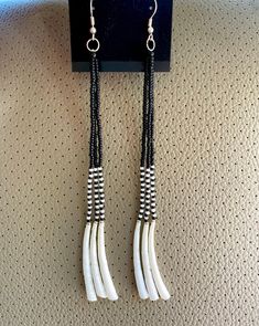 two white and black beads are hanging from a hook on a gray wall with silver earwires