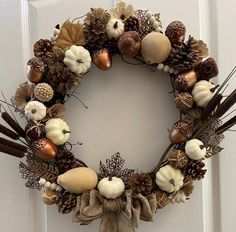 a wreath with pine cones, acorns and other autumn decorations hanging on a door