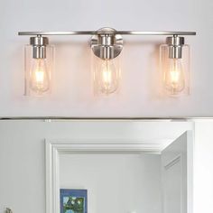 three light bathroom vanity fixture with clear glass jars on the front and back lights above it