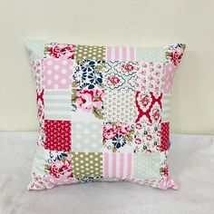 a pink and green patchwork pillow sitting on top of a white bed cover with polka dots