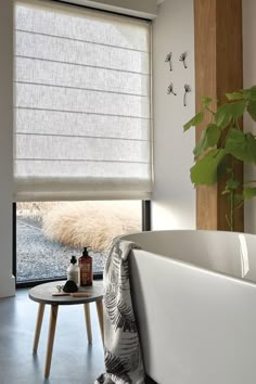 a white bath tub sitting under a window next to a table with a plant on it