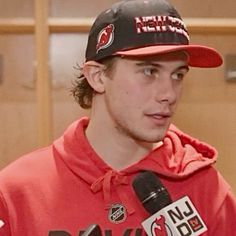 a man in a red hoodie is holding a microphone and wearing a black hat