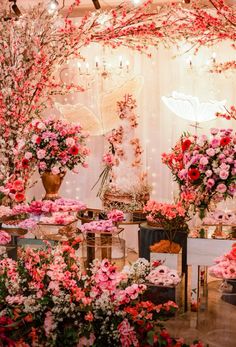 pink and red flowers are on display in front of a white backdrop with lights hanging from the ceiling