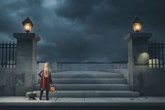 a woman in a red dress is standing on the steps with her dog and holding a pumpkin