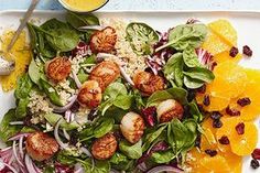 a salad with shrimp, oranges and spinach on a white platter next to a glass of orange juice