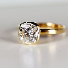 an engagement ring with a cushion cut diamond in yellow gold, sitting on a white surface