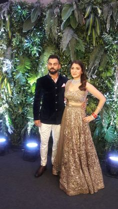 two people standing next to each other in front of a wall with plants on it